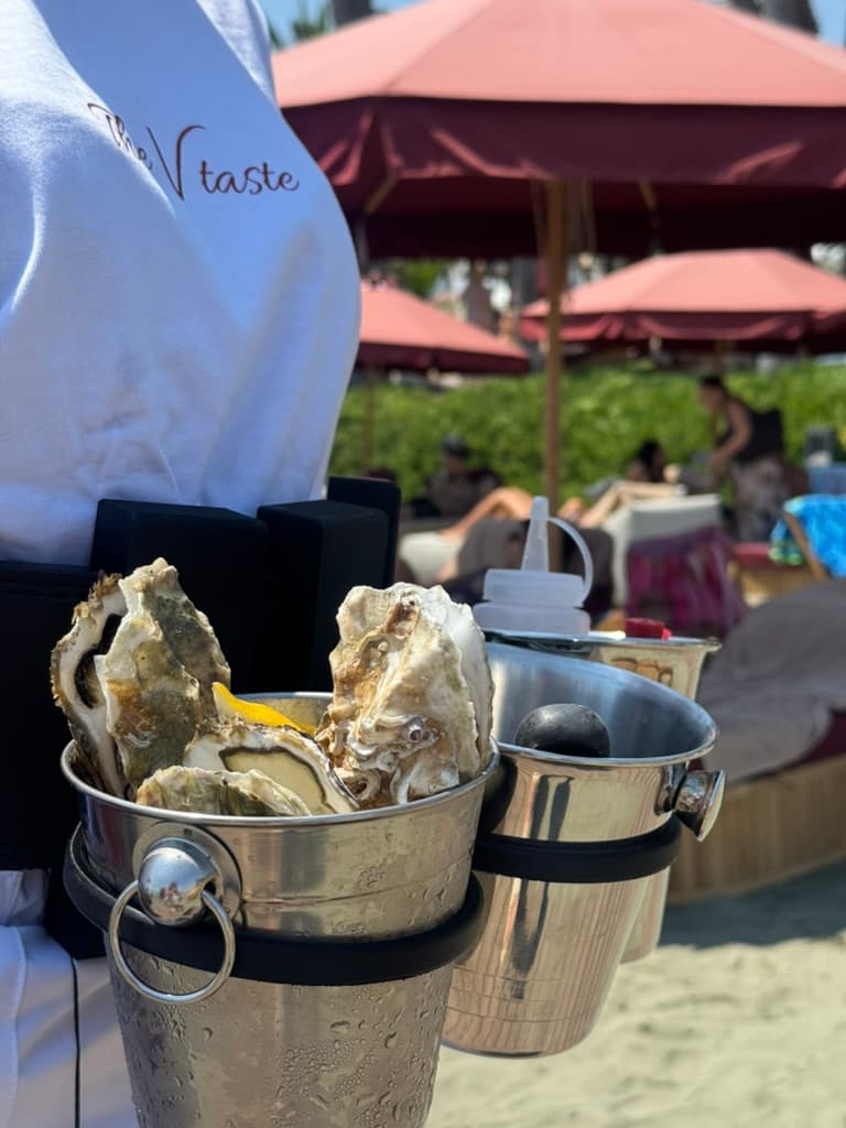 A TheVtaste server in branded uniform carrying oysters at a beachside event in Cyprus
